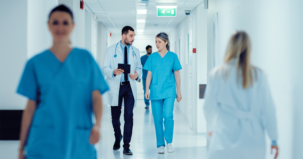 Male and Female Doctors Walk Through Hospital Hallway, They Consult Digital Tablet Computer while Talking about Patient's Health.