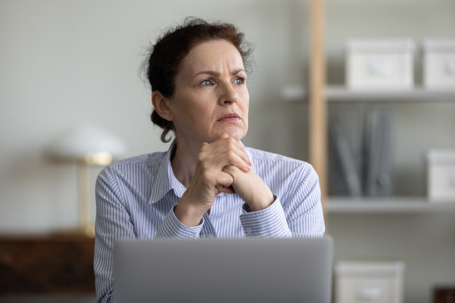 Concerned frustrated mature businesswoman sitting at laptop in office, looking away, thinking over challenging tasks.