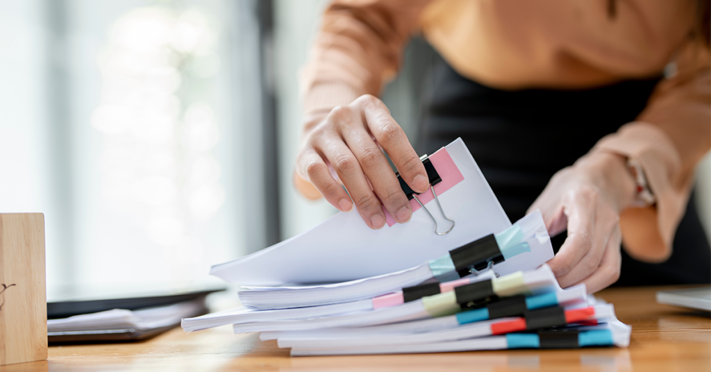 Businesswoman hands working in Stacks of paper files for searching and checking document achieves on folders papers at busy work desk office